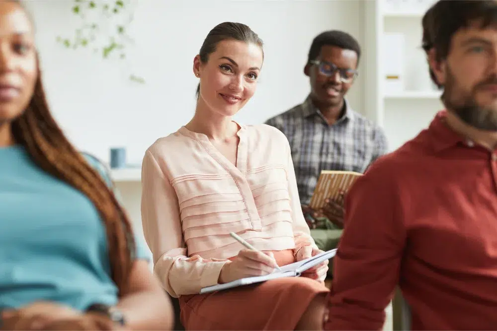 portrait elegant young woman smiling taking notes while sitting audience training seminar business conference office plans de retraite et d'épargne